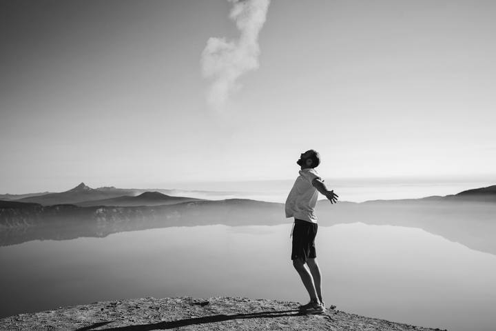 A person standing at a clifftop above a lake.