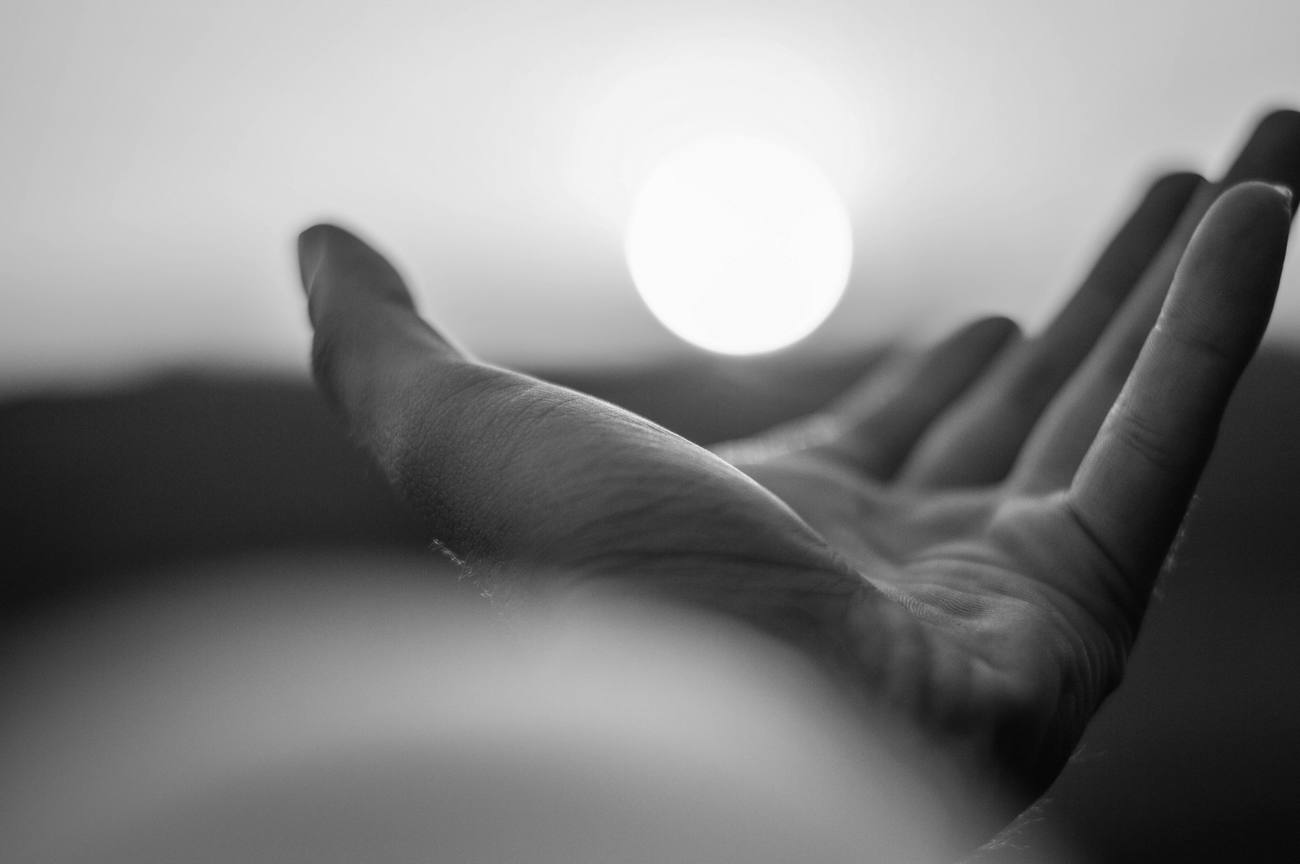 An open hand raised toward the light at dawn.