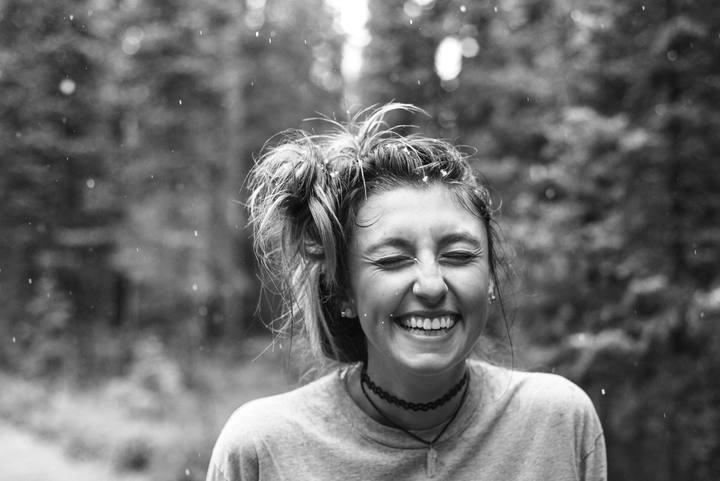 A person laughing outdoors among trees.
